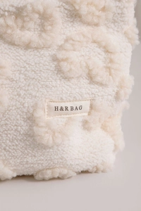 Close-up of a white plush makeup bag featuring a stitched H&R BAG logo label texture