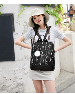 Close-up of black floral Oxford backpack with white pom-pom charm in outdoor setting