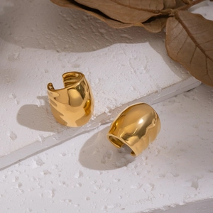 Polished gold geometric oval ear cuffs on textured stone with a natural leaf background