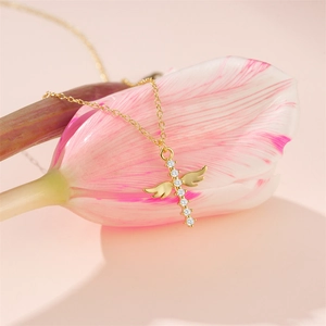 Macro detail of gold cross and angel wings pendant with white zircons on pink tulip
