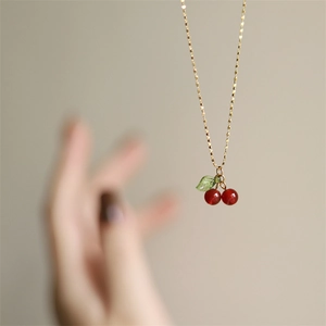 Macro detail of red cherry pendant necklace with green leaf and gold-plated chain