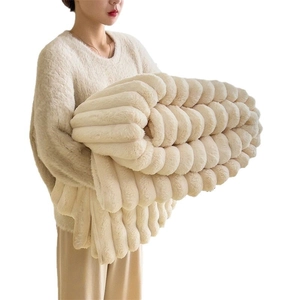 Thick cream faux rabbit fur blanket with wide ribbed texture held by a model