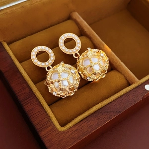Detail of gold hollow mesh sphere earrings with large pearls on brown velvet tray