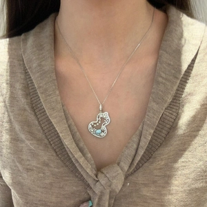 Macro detail of silver gourd pendant featuring blue gemstone and pearl on a dainty chain
