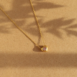 Minimalist 18K gold plated titanium necklace featuring a pink heart pendant on textured background