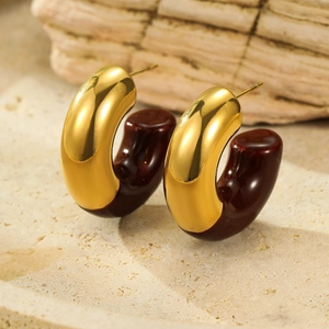 Macro shot of minimalist C-shaped gold and dark reddish brown resin earrings on stone