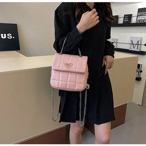 Detail of pink quilted crossbody bag with heart-shaped silver lock and chain strap on model