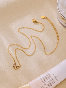 Detail view of a gold butterfly necklace with colored zircons on a beige textured surface