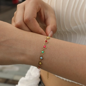 Detail view of a gold heart charm bracelet with colorful enamel inlay worn on the wrist