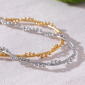 Macro shot of gold and silver snake chain necklaces with bead details on textured fabric
