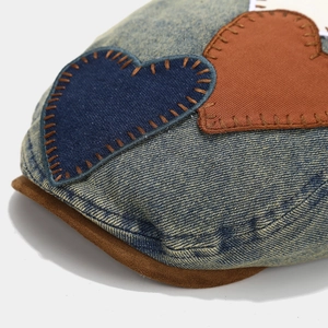 Close-up of denim beret texture with heart patches and brown stitched brim detail