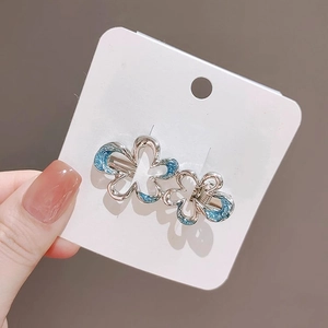 Hand holding silver floral hair clip with blue enamel detail on a white card display