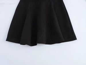 Detail of a black sleeveless mini dress featuring a smooth flared hem and fine woven texture