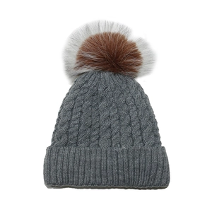 Detailed cable knit pattern on gray winter beanie featuring a large faux fur pom-pom