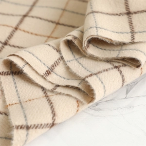 Close-up of soft beige plaid scarf fabric with brown and grey cross patterns and fringe