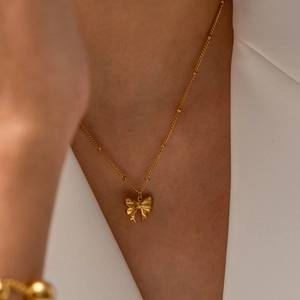 Elegant gold-plated stainless steel bow necklace on model with beaded chain detail