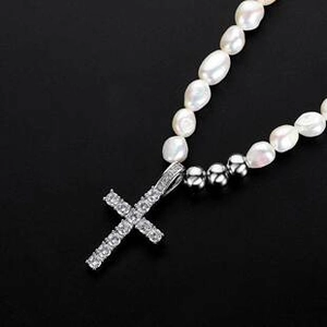Detailed close-up of a silver cross pendant with clear gems on baroque pearl necklace