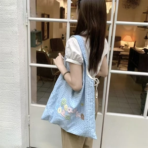 Detail of light blue checkered tote bag with colorful letter embroidery on shoulder