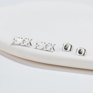 Minimalist silver 'FUCK' letter stud earrings on a white ceramic display plate