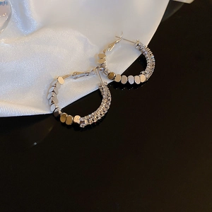Détails macro de boucles d'oreilles créoles argentées avec strass brillants et soie blanche