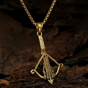 Detailed close-up of golden crossbow pendant with box chain on dark charcoal wood