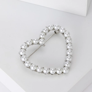 Detail of elegant heart brooch with white pearls and silver pin on a white surface