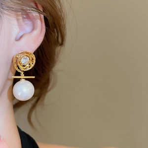 Close-up of pearl earring with gold swirl pattern and zircon on model ear
