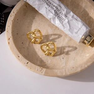 Detail of 18K gold stainless steel heart knot earrings on a beige stone display tray