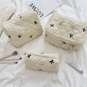 Three-piece quilted makeup bag set with black bow embroidery on off-white fabric