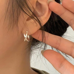 Close-up of minimalist silver crossover hoop earrings worn on ear for daily style