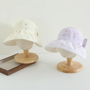 Detail of wide brim sun hats with floral print and bow tie on wooden stands