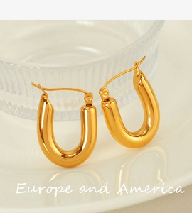 Close-up of polished golden U-shaped hoop earrings placed on a white ceramic plate