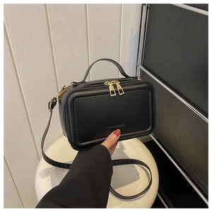 Detail of black suitcase-style crossbody bag with gold zippers and embossed fashion logo