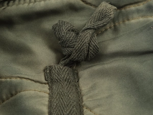 Detailed view of olive green jacket fabric texture with drawstring knot detail