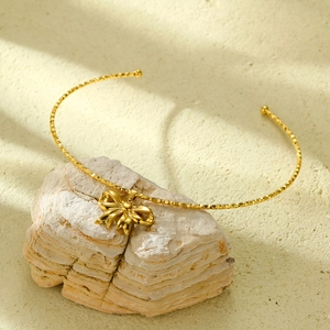 Detail of a gold bow pendant on a rigid collar necklace set against natural rocks