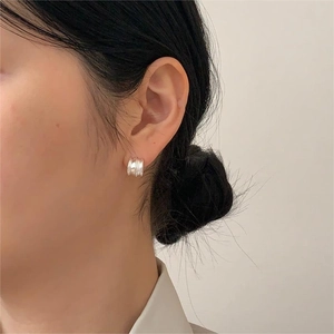 Macro detail of silver curved hoop earring with vertical ribbed texture on model ear