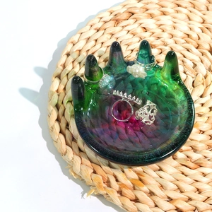 Detail van een handvormige glazen sieradenschaal met ringen op een rieten matje