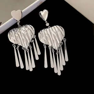 Silver wrinkled heart earrings with long metal tassels shown on a black background