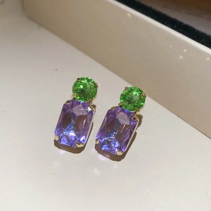 Macro detail of gold earrings featuring green round and purple square zircon stones