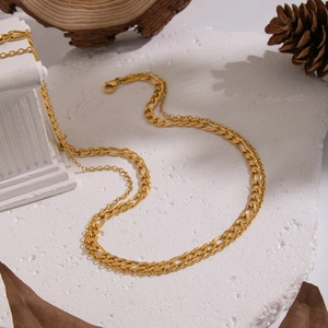 Double-layered golden stainless steel Cuban chain necklace on minimalist stone background