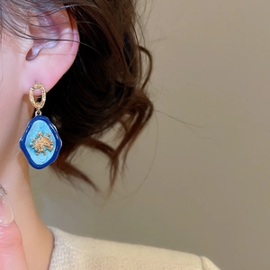 Gros plan de boucles d'oreilles fleurs en émail bleu avec bords dorés irréguliers