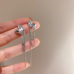 Close-up of silver heart drop earrings with long tassel chains and sparkling crystals