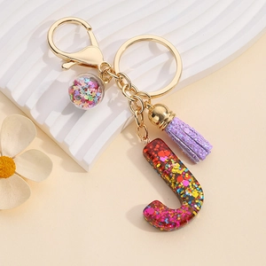 Detailed macro view of resin letter J keychain with purple tassel and colorful sequins