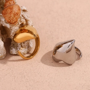 Close-up of heart-shaped gold and silver stainless steel rings on a sandy beach setting