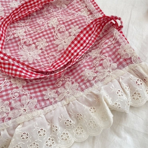 Close-up of red plaid canvas fabric with floral embroidery and white lace trim detail