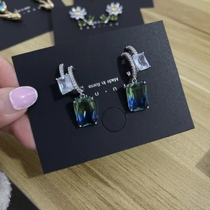 Detail of luxury S925 silver earrings with blue-green gradient crystals on black card