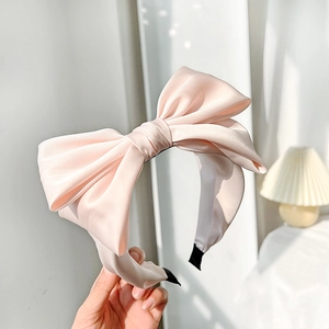 Detail of pink satin bow headband featuring a smooth texture and elegant oversized design