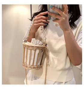 Detail of woven straw bucket bag featuring a large pearl handle and golden chain strap