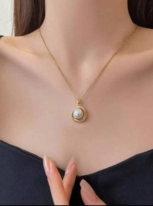Dettaglio di modella che indossa una collana dorata con ciondolo di perla e cristalli