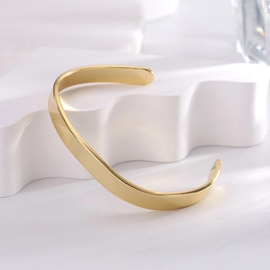 Minimalist gold-plated irregular brass cuff bracelet displayed on a wave stand